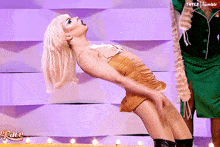 a woman in a gold dress is dancing in front of a purple wall with the word grace on it