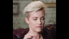 a woman with short blonde hair is sitting on a red leather couch .