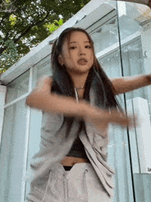 a woman in a grey vest and white pants is dancing in front of a glass door .