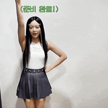 a woman wearing a white tank top and a black skirt stands with her arm up