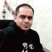 a man wearing a black hoodie with a white logo on the front looks at the camera