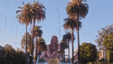 a woman in a yellow skirt is standing in a car surrounded by palm trees