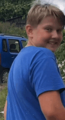 a young boy in a blue t-shirt is smiling while standing in front of a blue van .