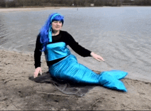 a woman in a mermaid costume is sitting on the beach near the water