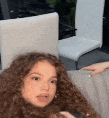 a girl with curly hair is sitting on a couch with her mouth open