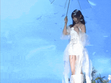 a woman in a white dress holding an umbrella in front of a blue background