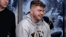 a man with a beard is wearing a gray hoodie with the letter e on it .
