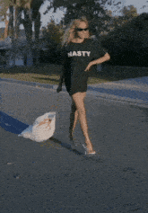a woman wearing a t-shirt that says nasty is walking down the street
