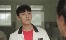 a young man wearing a red shirt and a white lab coat has a name tag that says ' a ' on it