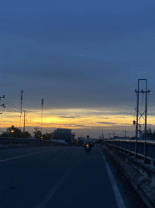 a person riding a motorcycle down a road with a sunset in the background