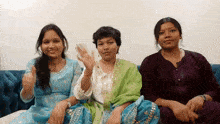three women are sitting on a blue couch and one is waving