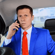 a man wearing a blue suit and red tie is talking on a cell phone