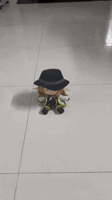 a stuffed animal wearing a black hat is sitting on a tiled floor