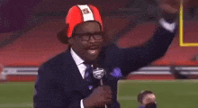 a man in a suit and tie is holding a microphone and wearing a red hat .