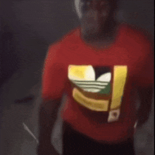a man wearing a red adidas t-shirt is standing in a dark room