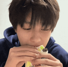 a young man in a blue hoodie is eating a piece of food