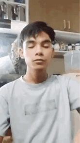 a young man is standing in a kitchen with his eyes closed and wearing a white shirt .