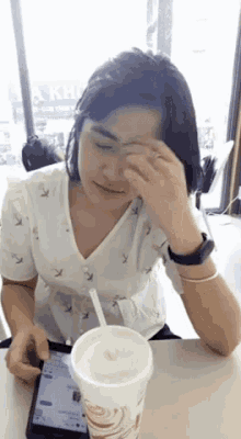 a woman sitting at a table with a cup of milkshake and a cell phone