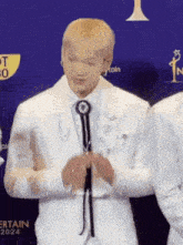 a man in a white suit and tie is holding a microphone .