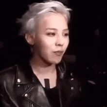 a young man with blonde hair is wearing a black leather jacket and making a funny face .