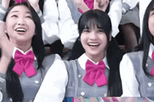 a group of girls wearing school uniforms and pink bow ties are sitting in a row .