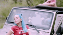 a woman with blue hair is standing in front of a jeep with the top down .