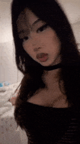 a woman with long dark hair and a choker is taking a selfie in a bedroom .