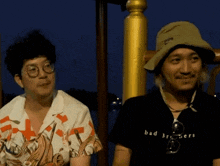a man wearing a black shirt that says bad brothers sits next to another man