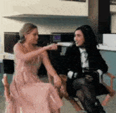 two women are sitting in chairs talking to each other and one is pointing at the other .