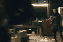 a man in a mask is standing in a dark room with a table and chairs .