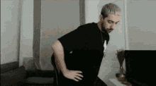 a man in a black shirt is standing with his hands on his hips in a living room .
