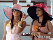 two women wearing hats are standing next to each other and one of them is saying " damn "