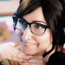 a woman wearing glasses and headphones is smiling with her hand on her chin