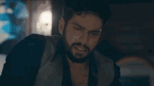a man with a beard is sitting in a dark room looking at something .