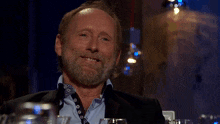 a man with a beard is smiling and sitting at a table with glasses