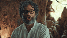 a man with curly hair and glasses is making a surprised face