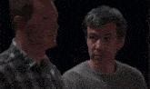 a man in a plaid shirt is talking to another man in a gray sweater