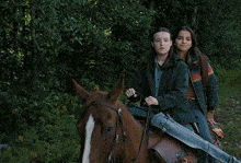 two girls are riding a horse and one has a rifle on her back