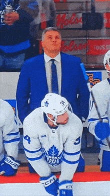 a man in a blue suit and tie stands behind a hockey player wearing a jersey that says toronto maple leafs