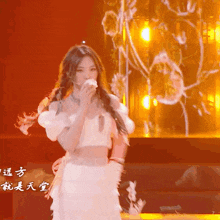 a woman in a white dress is dancing on a stage with chinese writing behind her