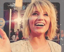a woman with blonde hair is laughing and waving her hand