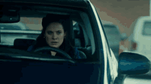 a woman is driving a car in a parking lot and looking out the window