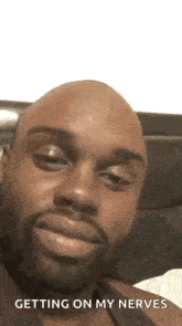 a bald man with a beard is making a funny face while sitting on a bed .