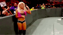 a woman in a pink top and shorts is standing on a wrestling ring .