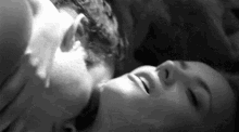 a black and white photo of a man and woman kissing while laying down .