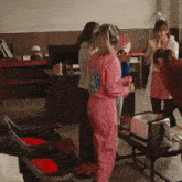 a woman in a pink jumpsuit with a blue logo on the back stands in a room with others