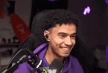 a young man in a purple hoodie is laughing in front of a microphone while sitting in a chair .
