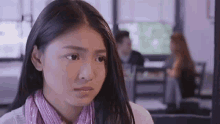 a young woman is sitting at a table in a restaurant looking at the camera with a sad look on her face .