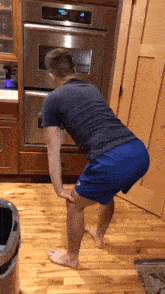 a man in blue shorts is squatting in front of a stainless steel oven that has the time of 4:20 on it