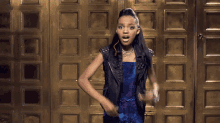 a young girl in a blue dress and black vest is dancing in front of a gold door
